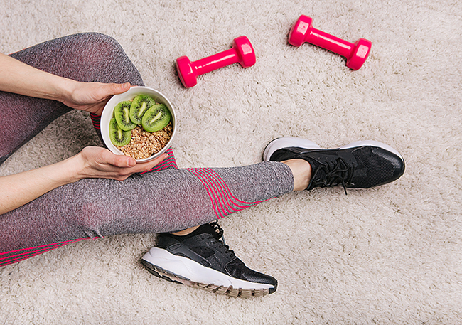 girl holds plate with muesli kiwi after fitness workout with dumbbells