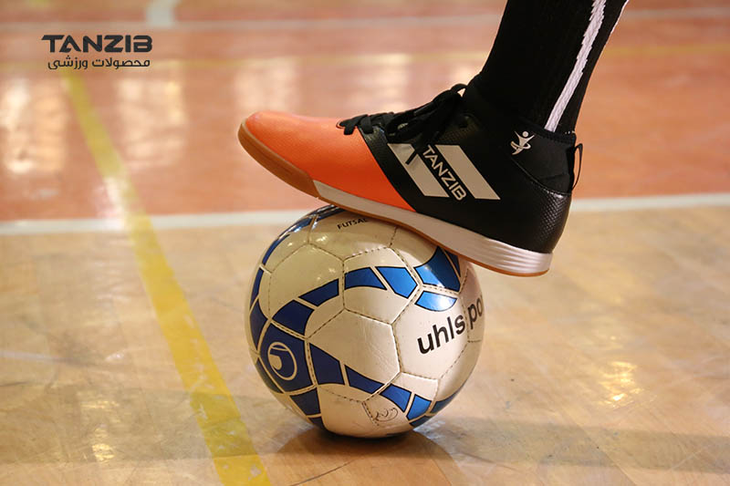 عکسی از بازیکن فوتسال که پای خود را همراه کفش مناسب فوتسال روی توپ قرار داده است. 