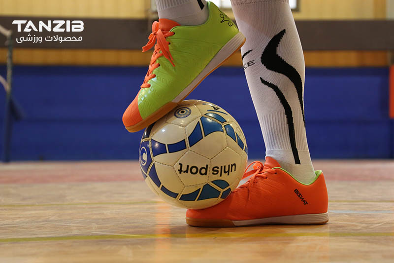 عکس از بازیکن فوتسالی که با کفش مناسب فوتسال و جوراب در حال بلند کردن توپ است با لوگوی تن زیب
