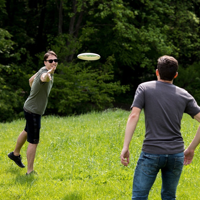 2 نفر در حال بازی با فریزبی با فریزبی تن زیب مدل پره ای در فضای سبز با بک درخت