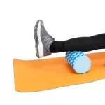 پسر ورزشکاری در حال تمرین با فوم رولر آجدار تن‌ زیب رو مت یوگا زیر یک پا از نمای نزدیک
