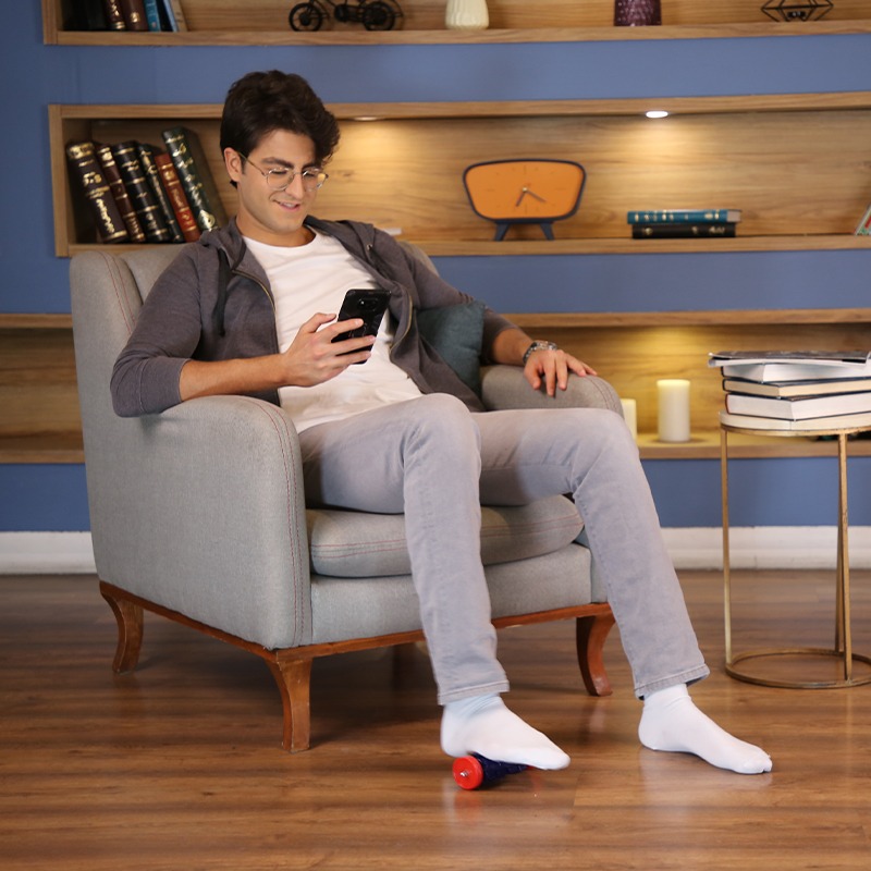 ماساژور رولی کف پا تن‌زیب مدل چرخ‌دنده‌ای زیر پای مدل پسری در حال کار با گوشی موبایل